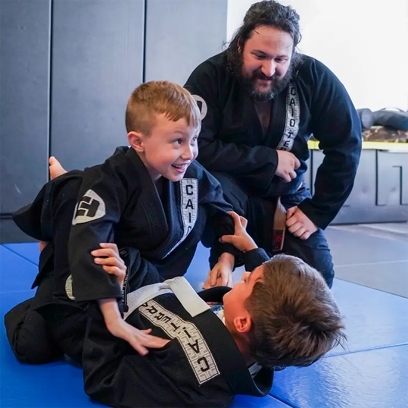 Kids practicing Brazilian Jiu Jitsu techniques in black gis while an instructor supervises at Caio Terra Academy Long Island.