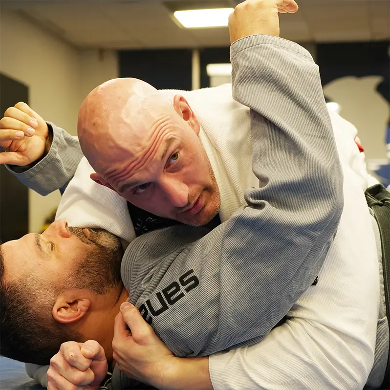 Two Brazilian Jiu Jitsu practitioners training a side control escape and shoulder pressure technique in a gi on the mat.