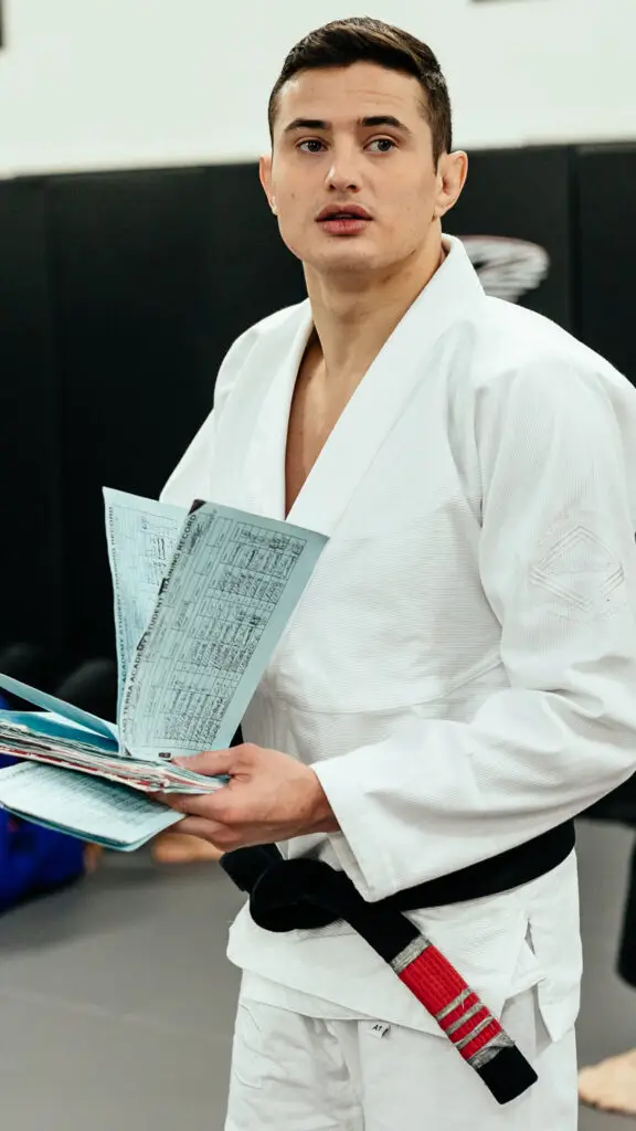 Brazilian Jiu Jitsu black belt instructor in white gi holding training records during class at Caio Terra Academy Long Island.