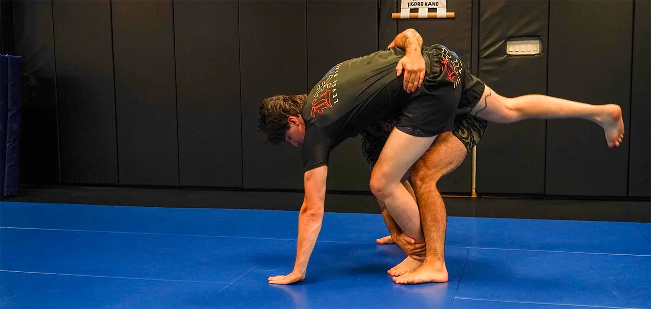 Two students practicing a takedown during a no-gi grappling class on blue mats at Caio Terra Academy Long Island.