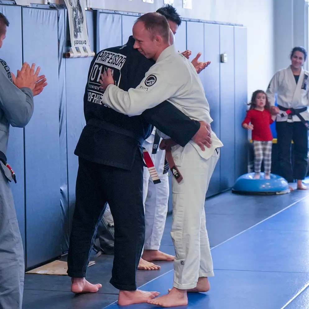 Brazilian Jiu Jitsu students embracing during belt promotion ceremony at Caio Terra Academy Long Island, surrounded by teammates.