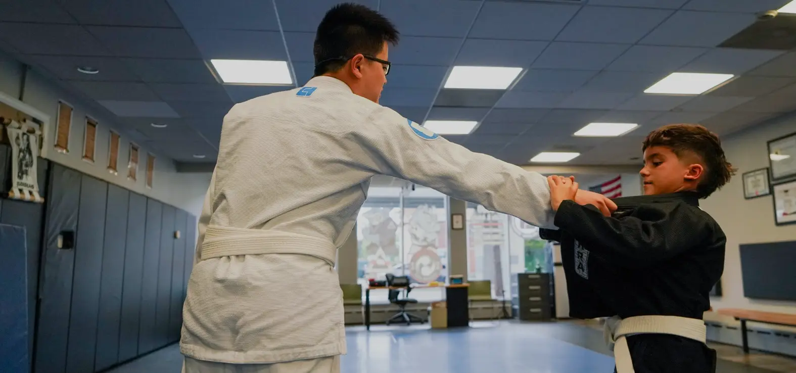 Two kids in Brazilian Jiu Jitsu class practicing grip techniques in white and black gis at Caio Terra Academy Long Island.